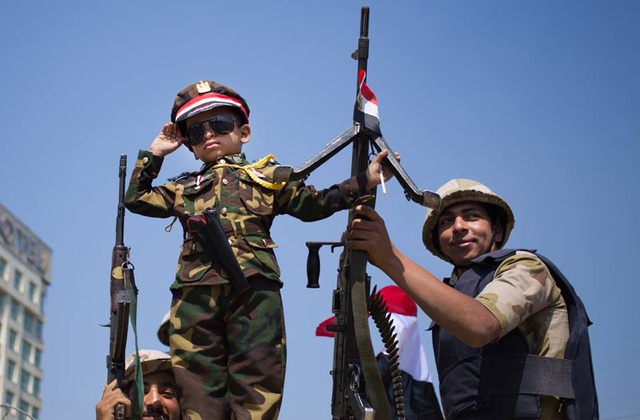Child dressed in military fatigue imitating Sisi.